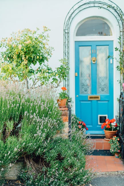 A well-maintained garden featuring a lush, green lawn with neatly trimmed grass and a circular flower bed in the center, bordered by small yellow flowers and two rounded, conical shrubs. Behind the fl
